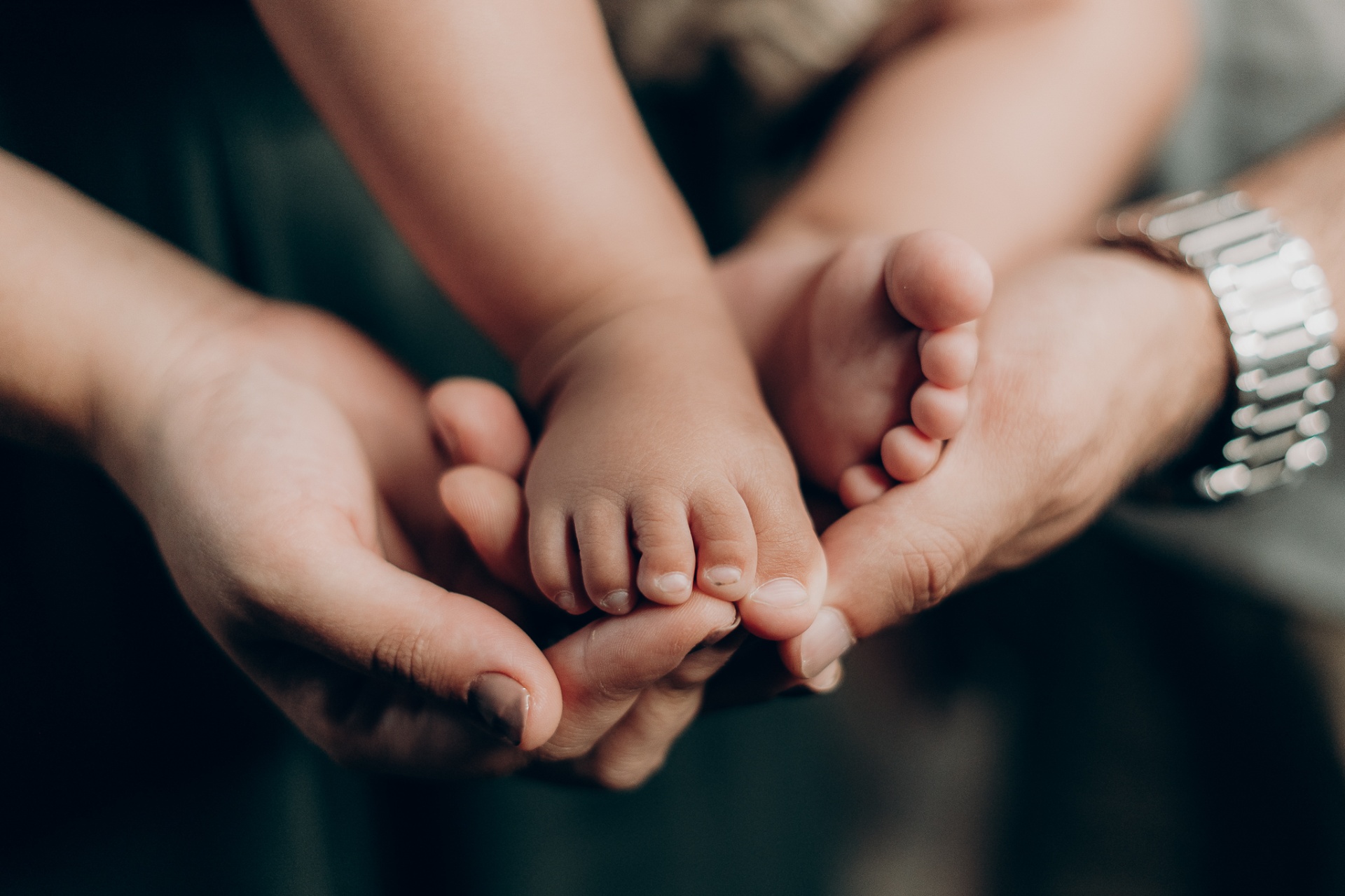 Mãos de pais acolhendo os pezinhos de um bebê — cuidado e afeto